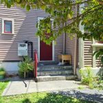 A shot of a sundrenched back door with a little bit of shade on three old stone steps by a wooden villa